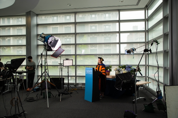Woman in black and orange robes behind a podium under TV lights