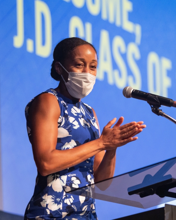 Woman in mask and printed sleeveless dress in front of microphone