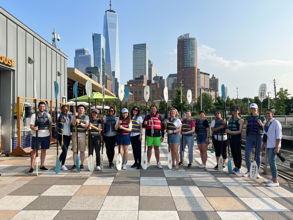 A group of Columbia Law students with kayak paddles and the NYC skyline behind them