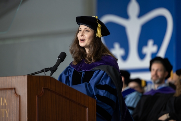 Woman with long dark hair in academic robe and tam speaks at podium