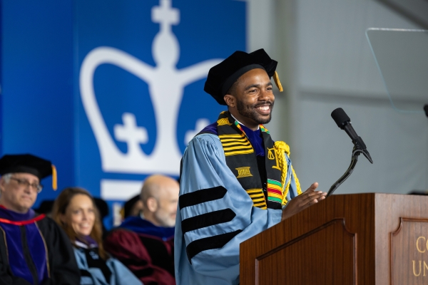 Smilling bearded man in tam and academic robe at podium