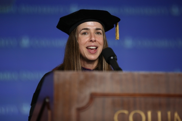 Woman with long hair and tam speaks at podium