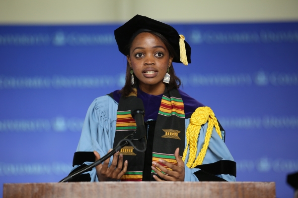 Woman in tam with tassel and academic robe with sash at podium