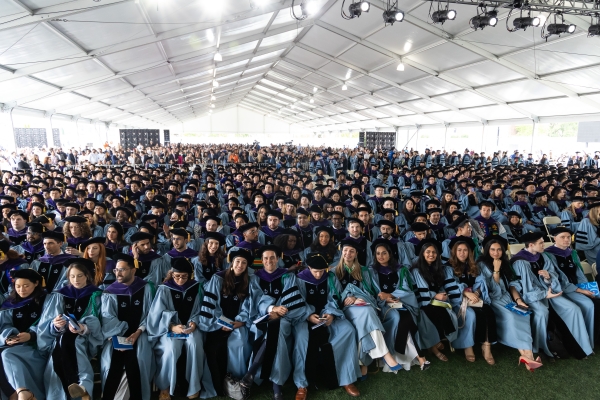 Students in academic regalia seated under enormous tent