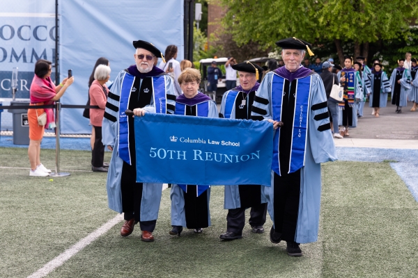 Four people in academic regalia carrying "50th Reunion" banner
