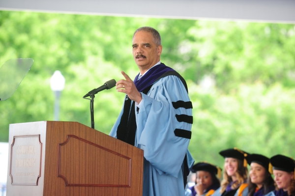 Eric Holder in academic robe speaking in front of a podium