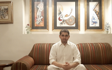 Man in a white shirt on a striped sofa in front of stained glass windows