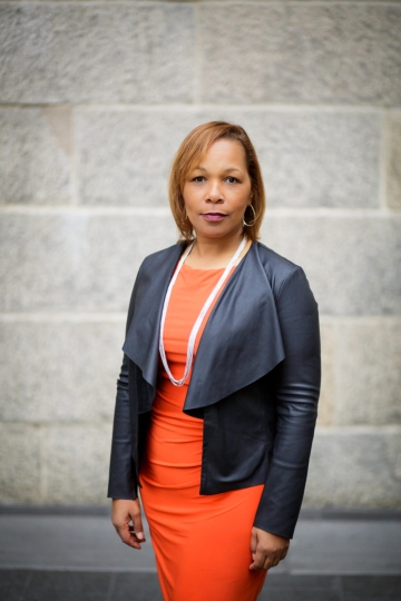 Woman in orange dress, pearls and gray jacket