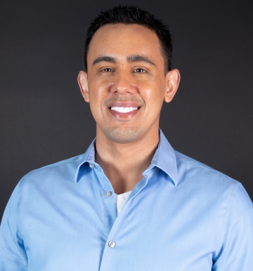 Photograph of man with short dark brown hair smiling and wearing a light blue button down