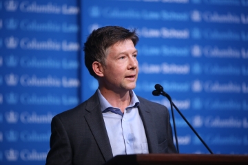 White man in gray jacket and blue shirt at podium 