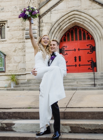 groom holds bride in arms on steps of church