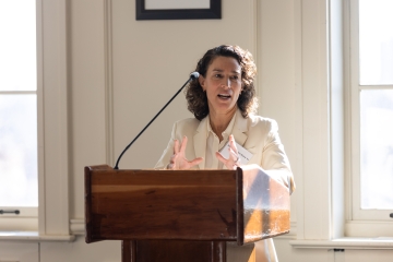 Woman in white jacket speaks at podium