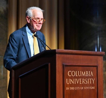 Professor Merritt Fox in a tie and jacket before a wood podium with the words Columbia University.