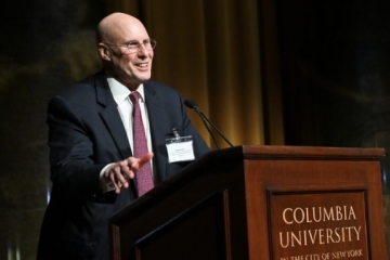 Professor Robert Smit in dark suit and red tie before a Columbia University podium